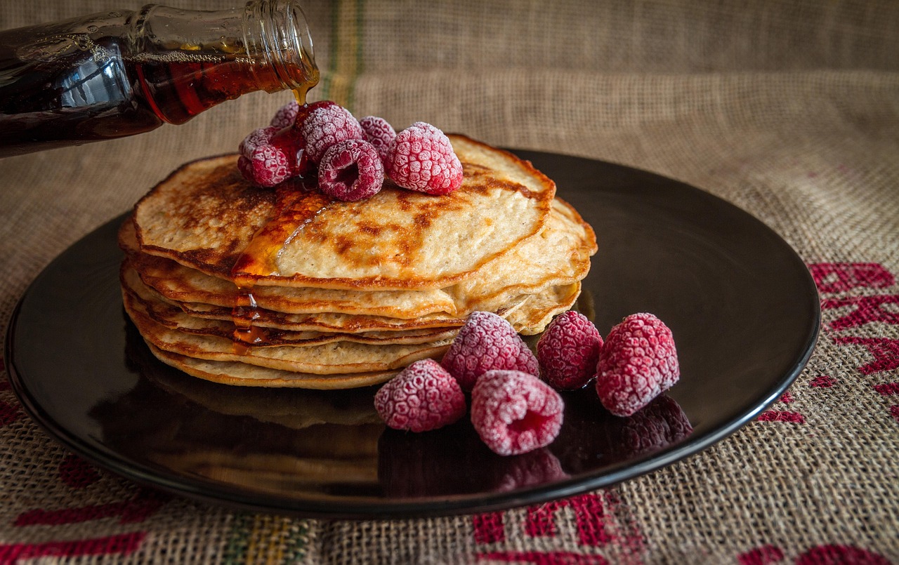 Syrup pouring over pancakes with raspberries